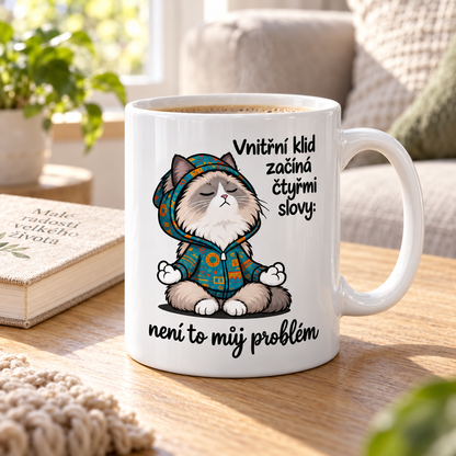 Lifestylová fotografie bílý keramický hrnek s meditující kočkou v mikině a vtipným nápisem Vnitřní klid začíná čtyřmi slovy: není to můj problém.“