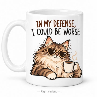Rendering of white ceramic mug with cartoon content maincoon cat saying "In my defence, I could by worse" on white background. Print on right side view.