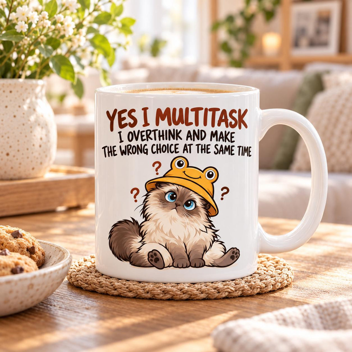 Rendering of white ceramic mug with cartoon confused ragdoll cat saying "Yes I can multitask. I overthing ane make the wrong choice" on wooden table.