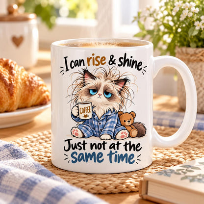 Rendering of white ceramic mug with cartoon sleepy ragdoll cat saying "I can rise & shine. Just not at the same time" on wooden table.