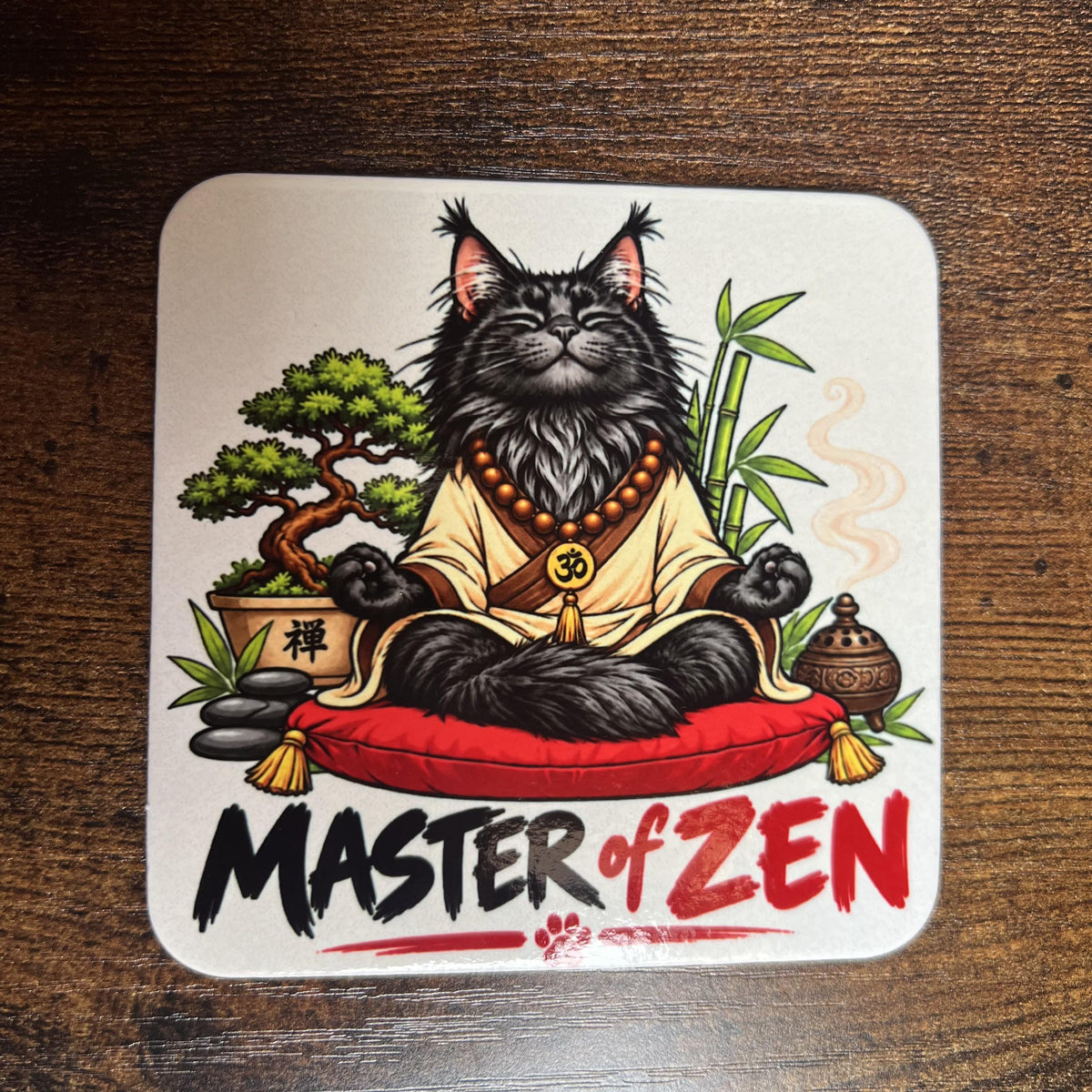 Korkový podtácek s kreslenou meditující černou mývalí kočkou říkající "Master of ZEN" na dřevěném stole. Pohled shora.
